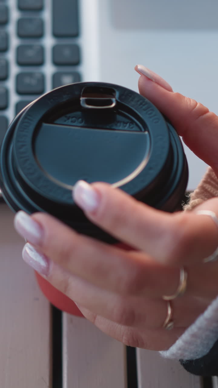 primer plano de la mano de la mujer con las uñas cuidadosas girando suavemente la taza de café cerca de la computadora portátil, centrándose en los dedos contra un fondo borroso del teclado