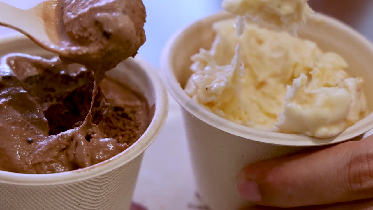 Una mano usa una cuchara de madera para servir helado de chocolate y vainilla en copas
