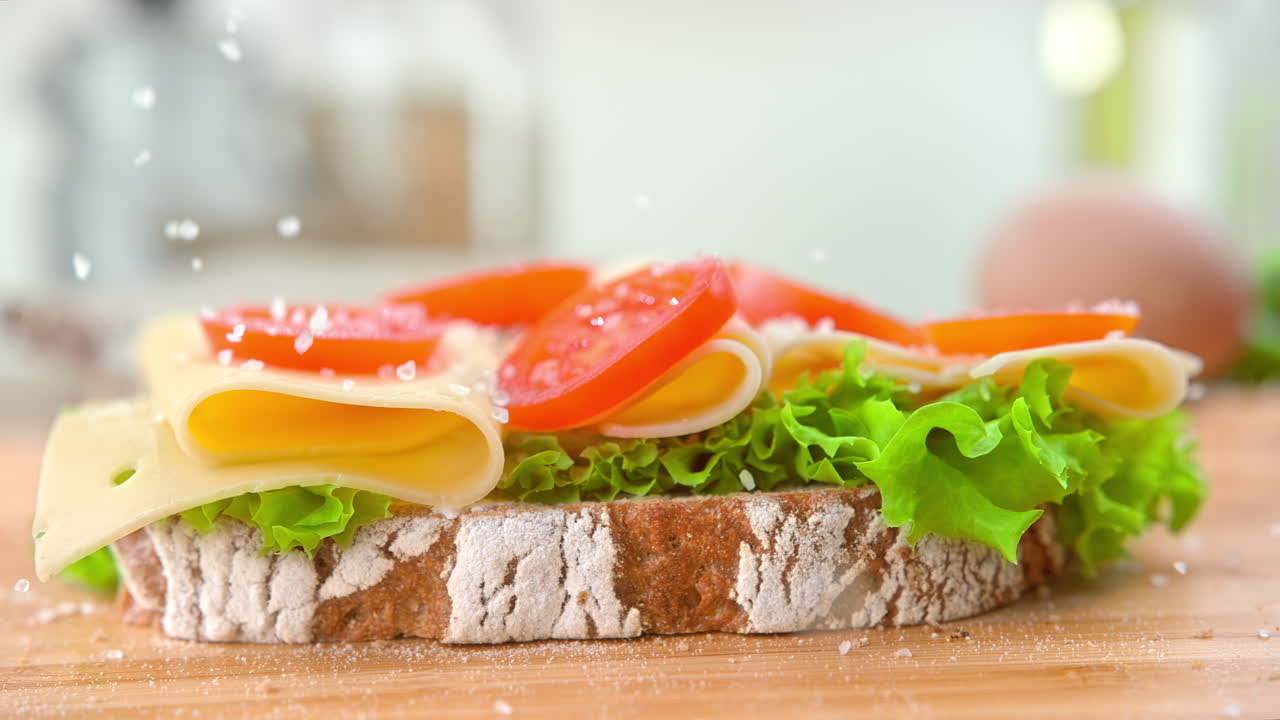 salar un sándwich hecho con pan blanco con lechuga rizada, queso y rebanadas de tomate - macro y cámara lenta
