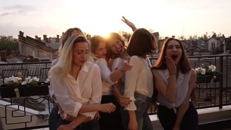 Close-up-of-fashionable-girls-in-the-same-casual-clothes-seductively-dancing,-posing-in-front-of-the-camera-on-the-terrace.-Evening-dusk