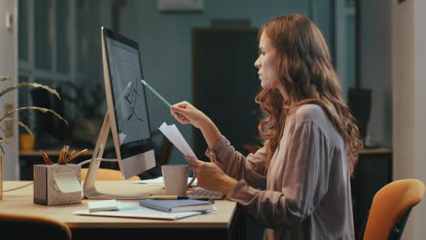 mujer de negocios enfocada trabajando con gráficos financieros en la pantalla de la computadora por la noche