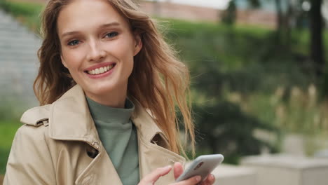 caucasian female student using smartphone and smiling outdoors.