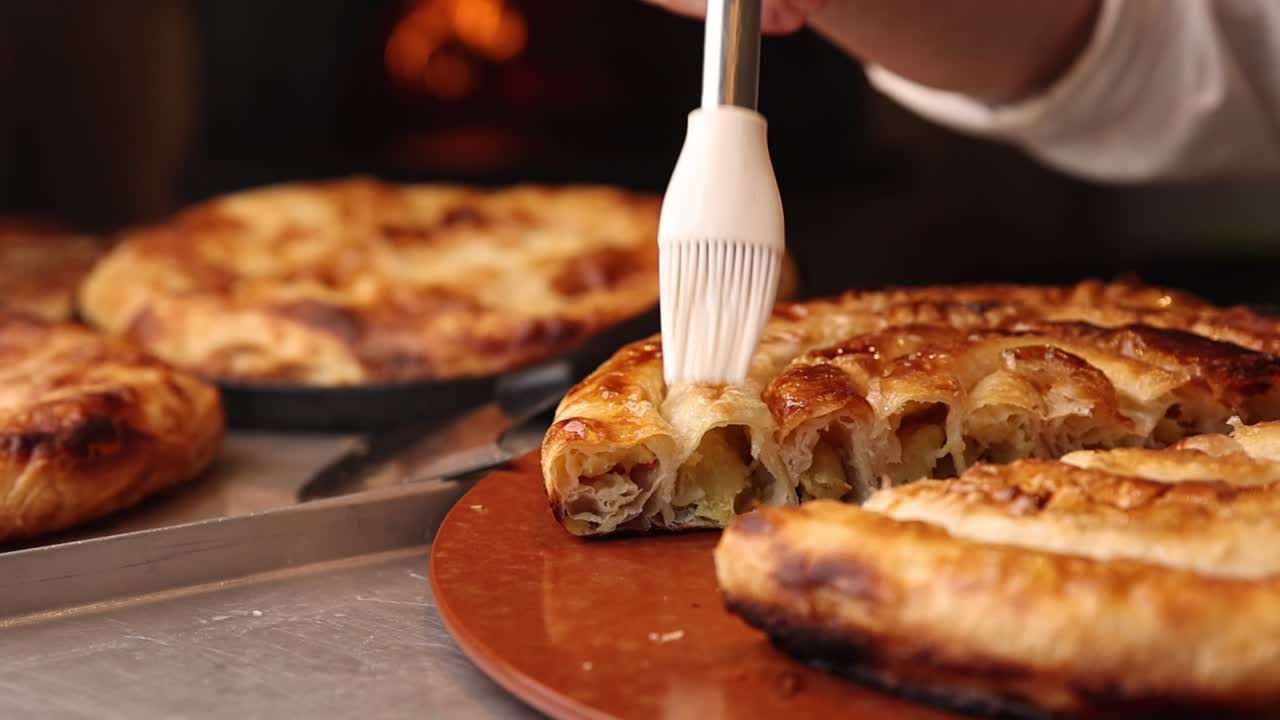 Chef che spennella con olio un burek tradizionale appena sfornato.