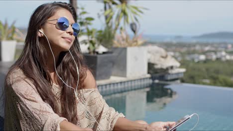 woman listening to music at poolside and enjoying sunny day