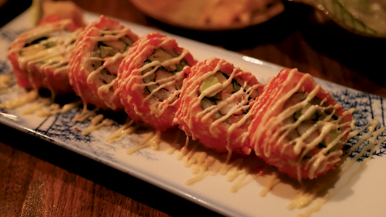 Sushi rolls with vibrant toppings on a decorative plate under warm lighting, showcasing intricate culinary presentation