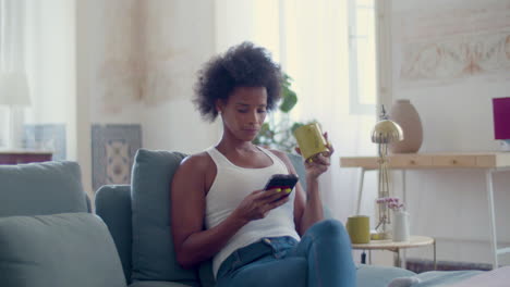 black woman drinking tea while using mobile phone