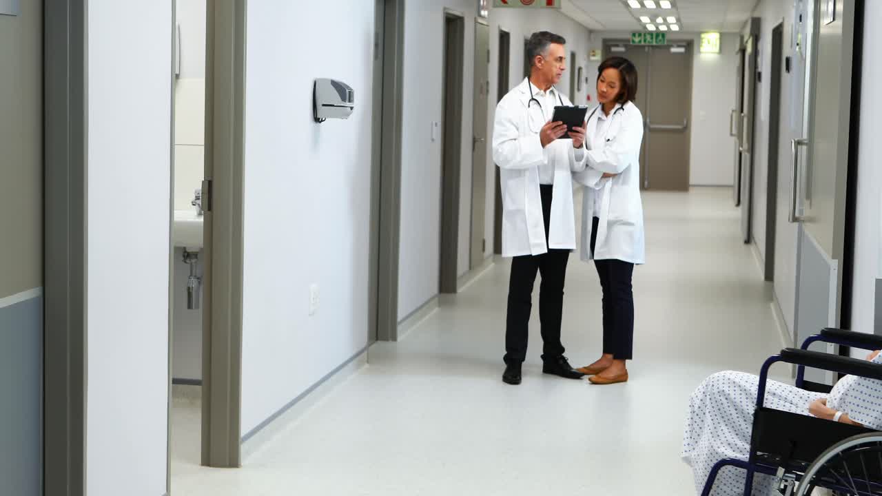 Mulher grávida sendo transportada em cadeira de rodas enquanto um médico conversa ao fundo.