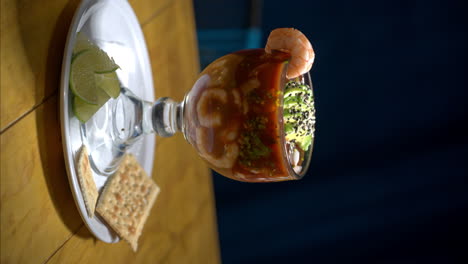 vertical shot of a traditional typical mexican seafood cocktail with shrimp and avocado served on a glass cup with crackers and lime slices