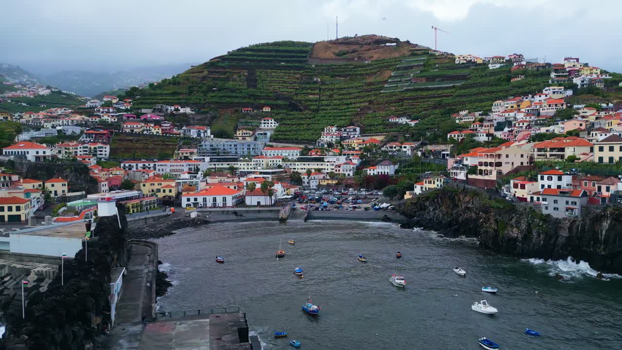 Vista aerea di piccole barche da pesca e del paesaggio costiero a Câmara de Lobos, Madeira, Portogallo, che mostra case sulla collina, vigneti terrazzati e un pittoresco paesaggio portuale