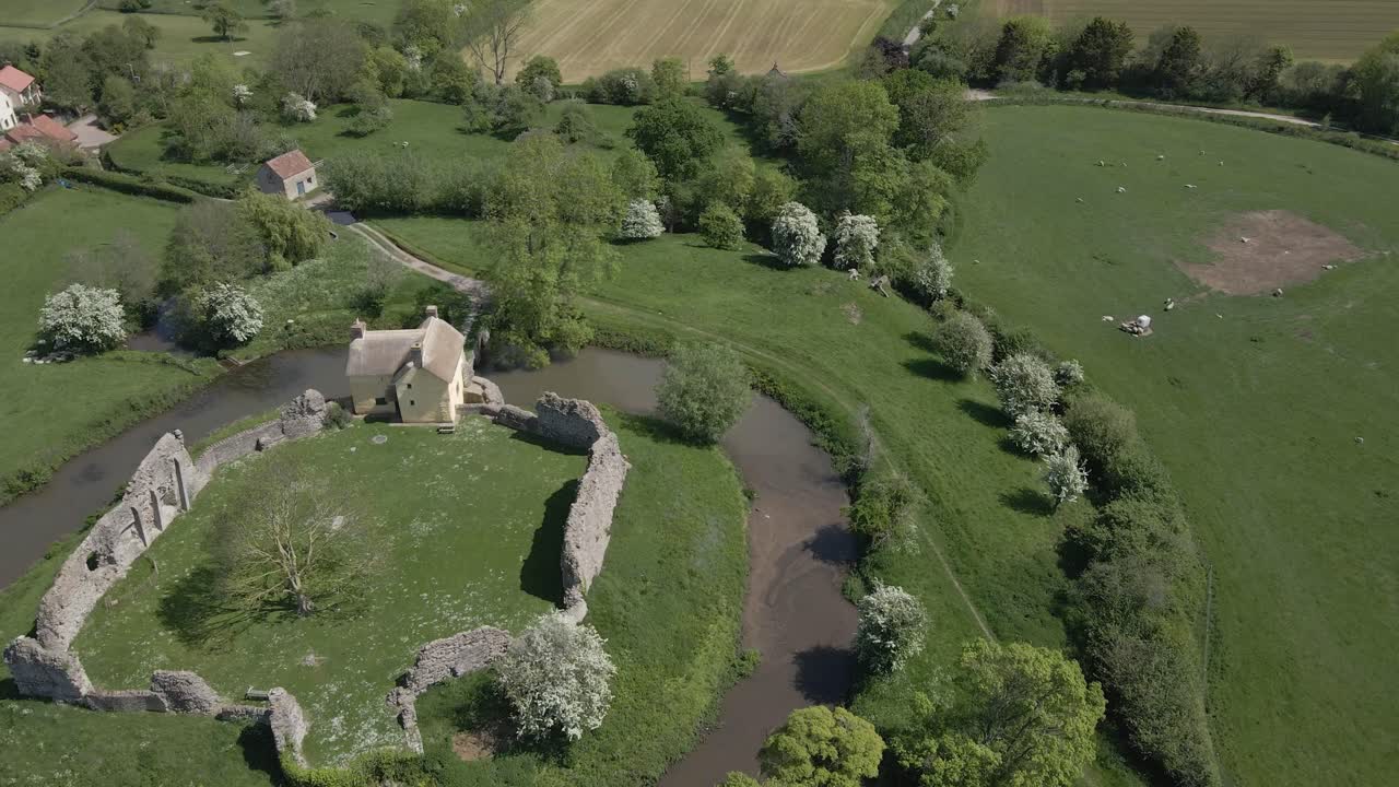medieval castle in Somerset, England. Most of the site is in ruins, with a thatched gatehouse used for holiday's. Drone rotating over the ruins and moat. 60fps, 4K