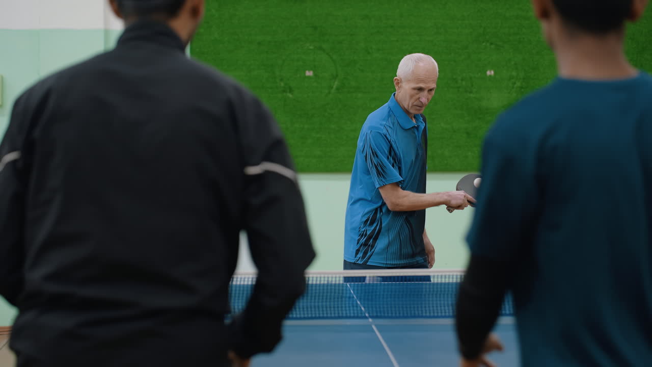 Close up back view of two athletes playing against senior coach during intense table tennis rally, one player misdirects shot into net while coach maintains focus in competitive indoor training match
