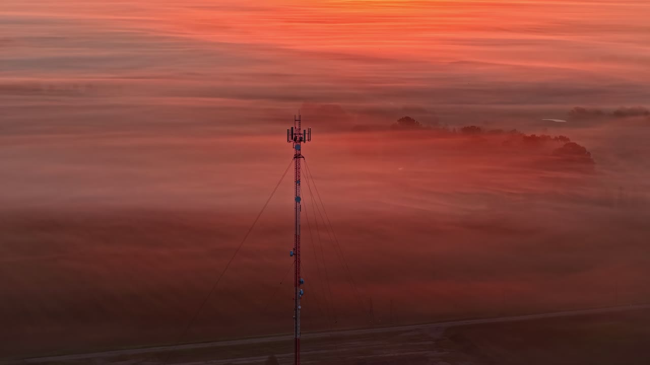 Mobilmast der rejser sig højt over et tåget landskab ved daggry.