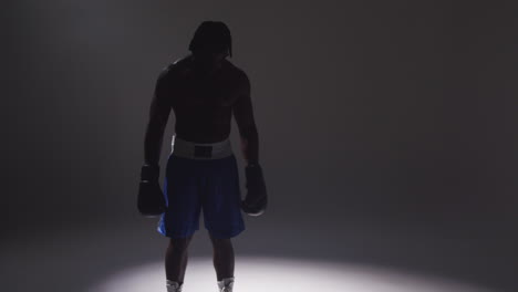 silhouetted studio shot with low key lighting of boxer wearing gloves standing in pool of light against grey background