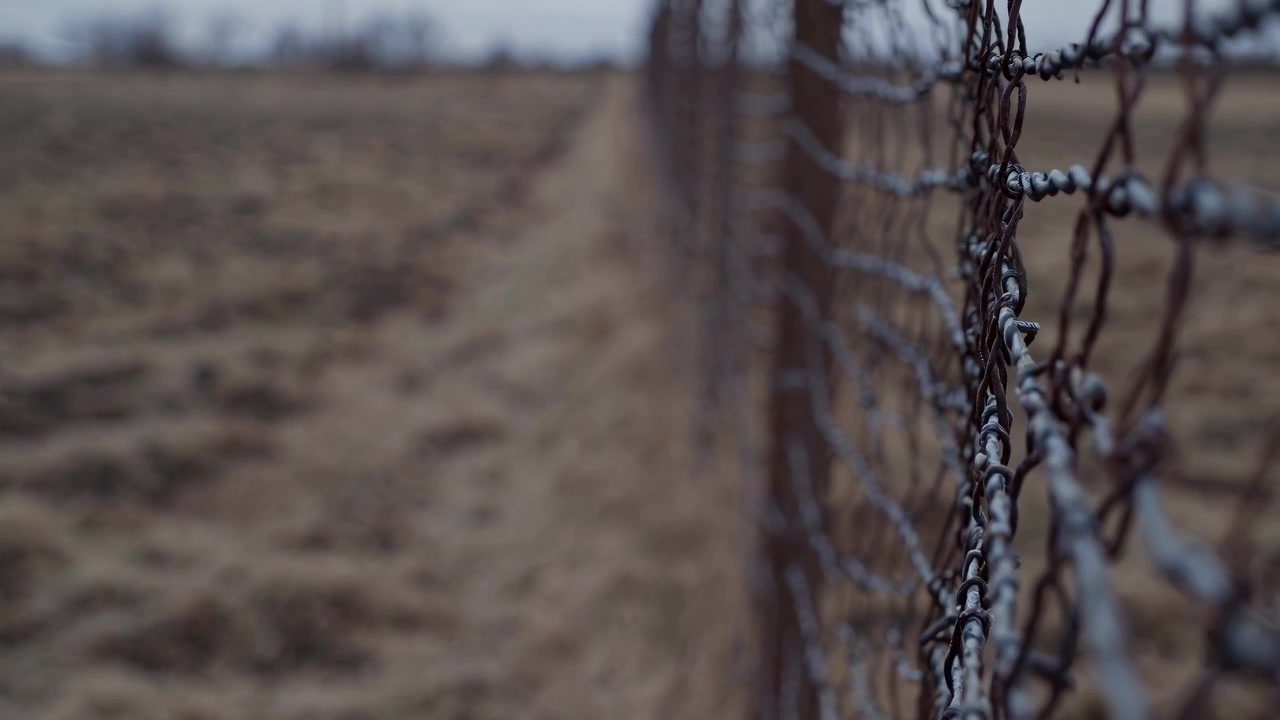 Rusty Barbed Wire Fence Along a Barren Field