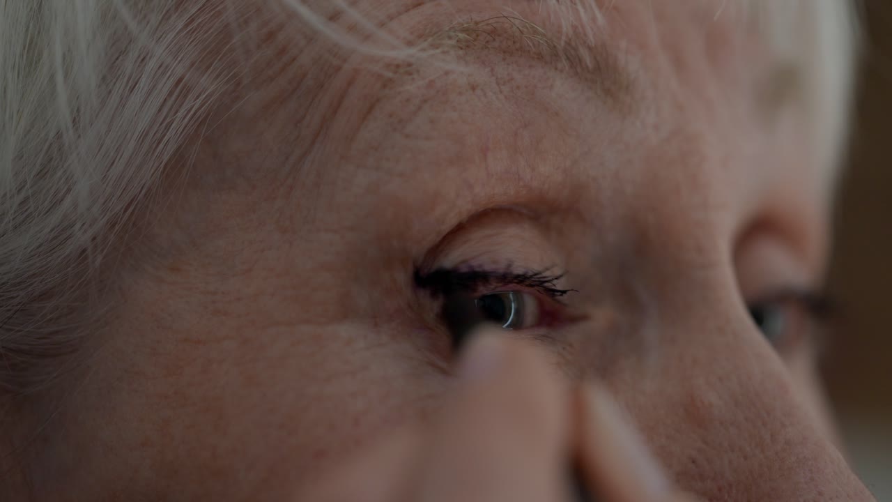 Close-up of an older woman applying makeup to her eye