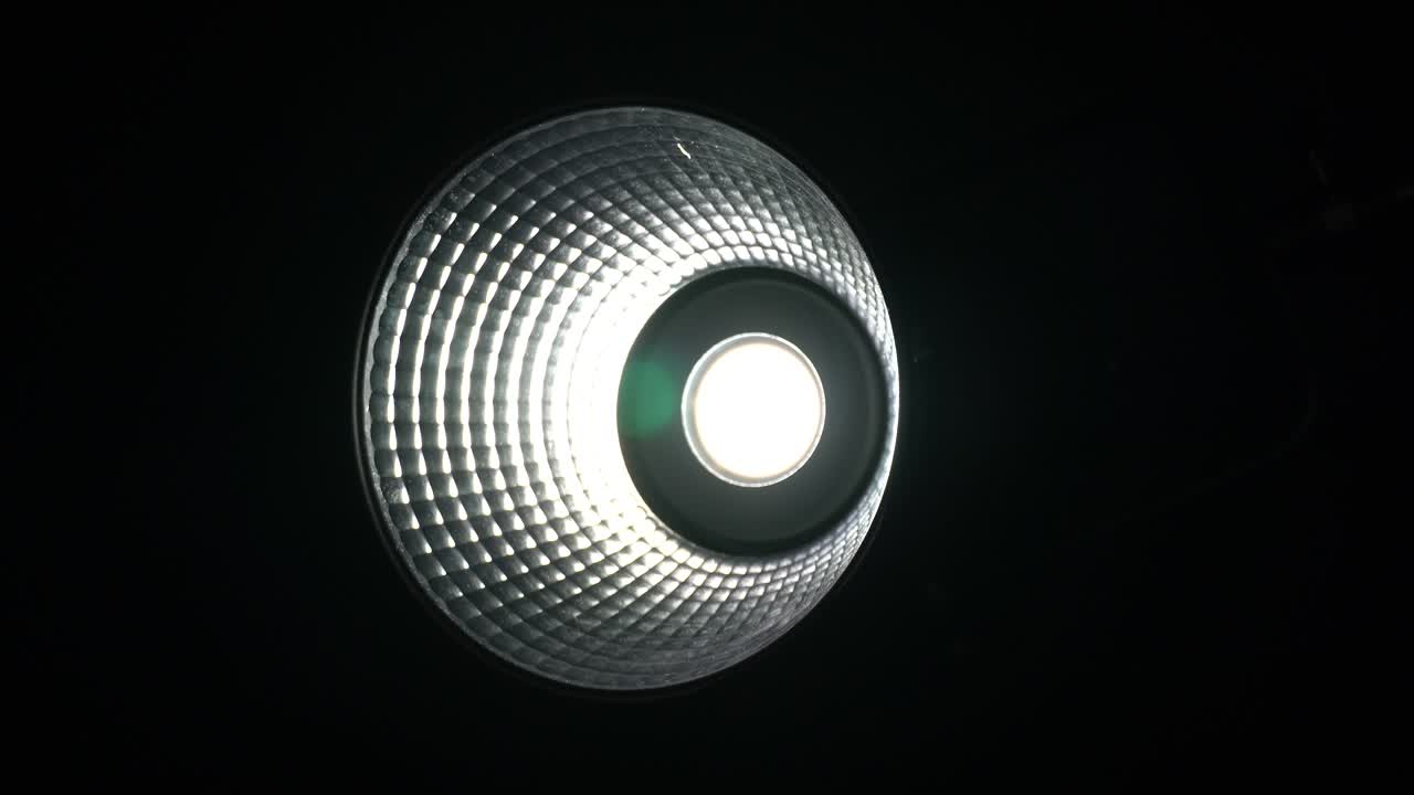Moving spotlight for cinema. Slow turn of video camera heavy duty lightning on black background. Professional light gear for production studio and movie footage.