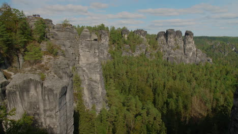 sandstone formations elbsandsteingebirge sachsen elbe rising above dense green forests mountains, under a blue sky with scattered clouds, showcasing the region’s natural beauty and rugged terrain
