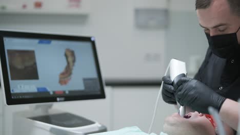 doctor scans the patient's teeth in the clinic. the dentist holds in his hand a manual 3d scanner for the jaw and mouth. dental health. creates a 3d model of teeth and gums on a medical monitor.