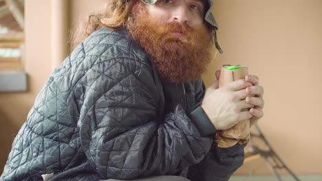 Homeless-Man-outdoors-in-blue-jacket-holding-beer-can-with-two-hands-looking-around-candid-moment