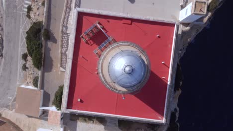 witness breathtaking aerial views of the cap de formentor lighthouse perched on the cliffs of mallorca. the vibrant red roof contrasts beautifully with the blue mediterranean sea.