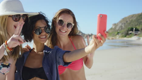 group of girl friends taking selfies on the beach making peace sign using pink phone