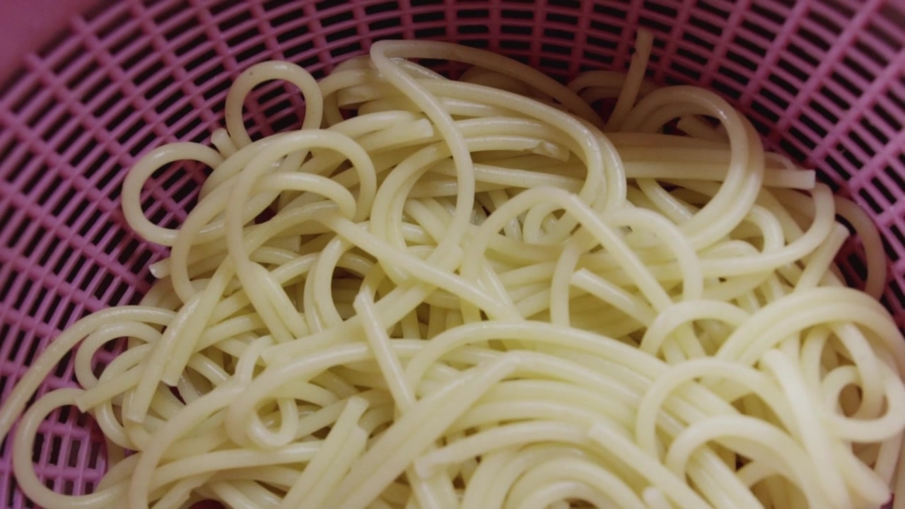 Primo piano di spaghetti cotti in uno scolapasta rosa. Ideale per tutorial di cucina, contenuti di cucina italiana e video di preparazione dei pasti