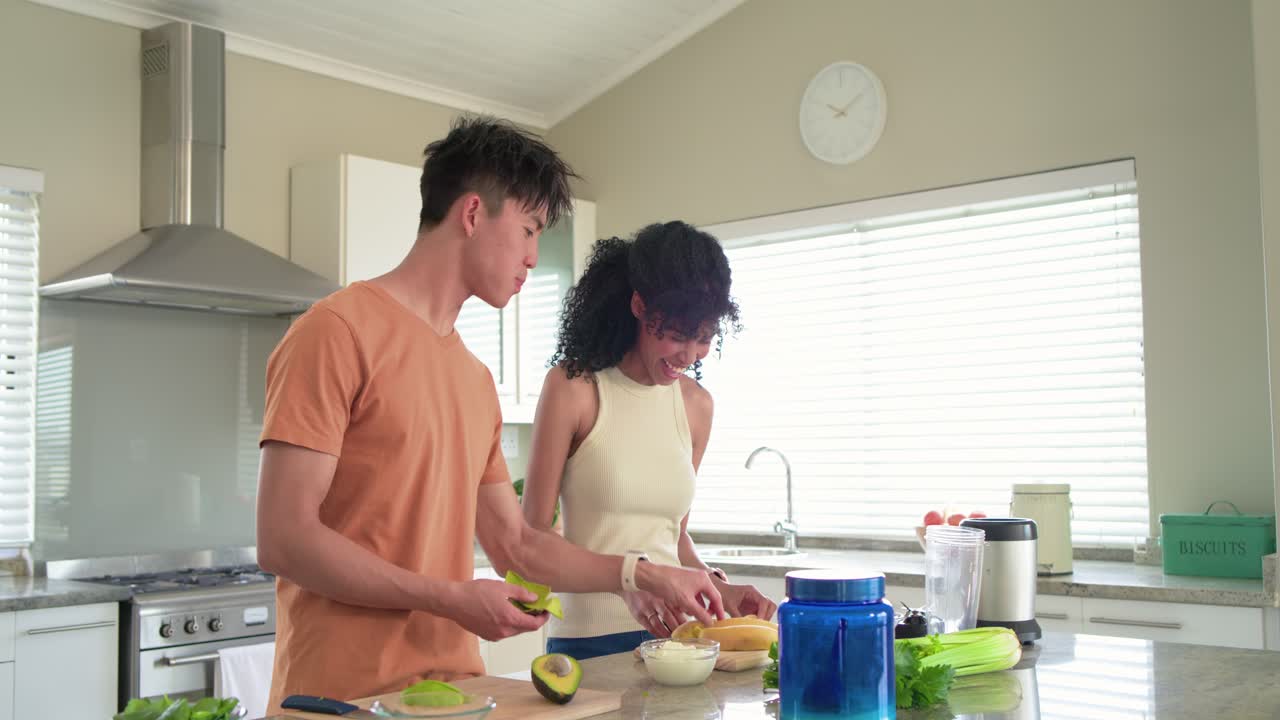 Coppia che taglia l'avocado al bancone della cucina, l'uomo si china offrendo un morso, la donna che gli dà da mangiare e che finisce la preparazione del pasto.