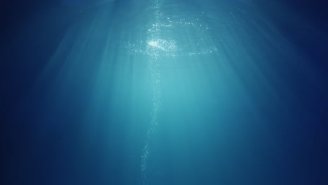 rayos de luz solar bajo el agua que brillan desde arriba atravesando el agua azul cristalina profunda causando una hermosa cortina de reflejos de iluminación de agua con burbujas de aire que suben a la superficie