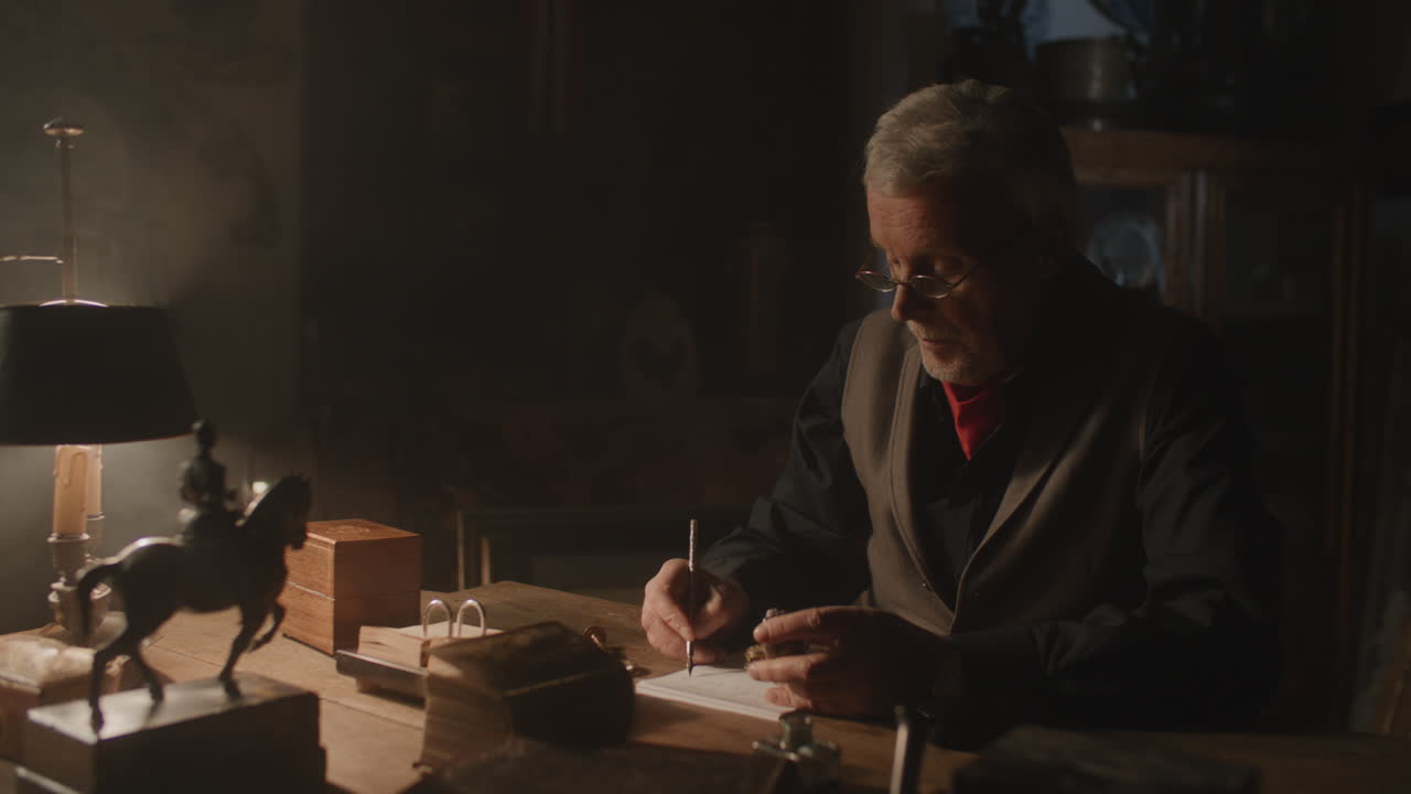 Older passionate man evaluates an old silver skull watch in his office at night