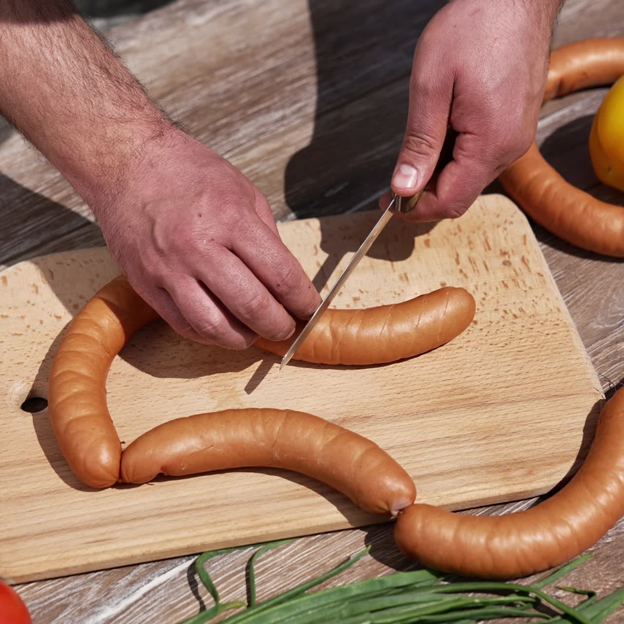Uomo che taglia le salsicce prima di grigliarle. Chef che pratica incisioni sulle salsicce per hot dog per un picnic all'aperto. Cucinare e mangiare nella natura. Vista dall'alto.