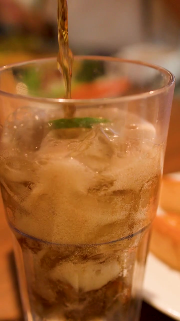 Versare cola in un bicchiere con ghiaccio e lime.