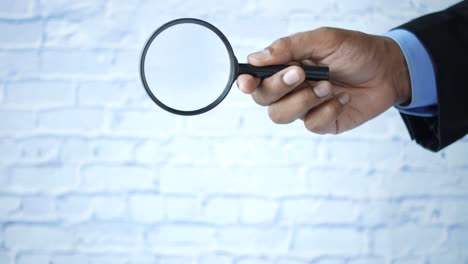 Hand-holding-magnifying-glass-against-white