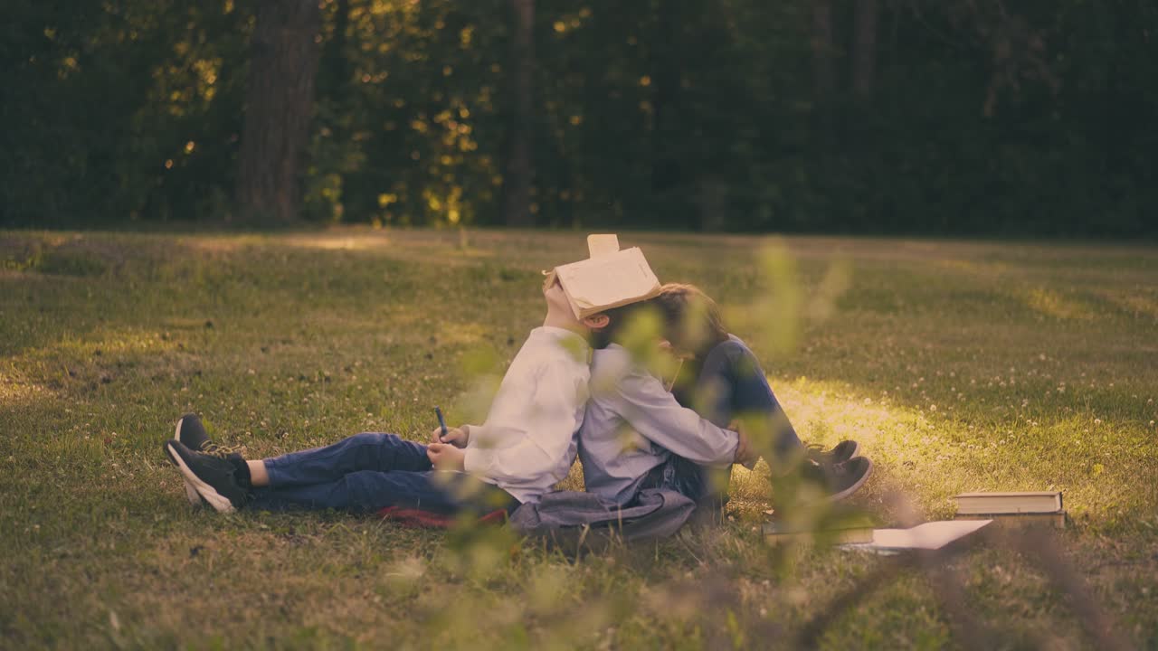 교과서를 가진 소년들은 시험 준비에 지쳐 잔디에 휴식을 취합니다.