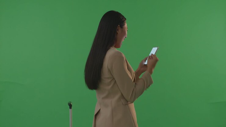 задний вид азиатская бизнесменка путешественник с багажем кричит цель празднует во время использования смартфона в зеленом экране фона студия, во время захода солнца