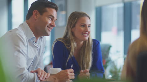 Close-Up-Of-Business-Team-Having-Meeting-Sitting-Around-Table-In-Modern-Open-Plan-Office