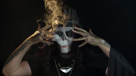 man in skeleton halloween creepy skull makeup exhaling cigarette smoke from his mouth, smiling