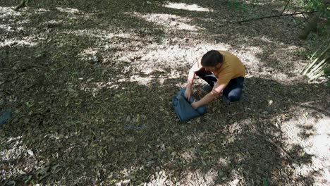 persona enrollando tela de carpa en un rollo pequeño para continuar la caminata en el área boscosa