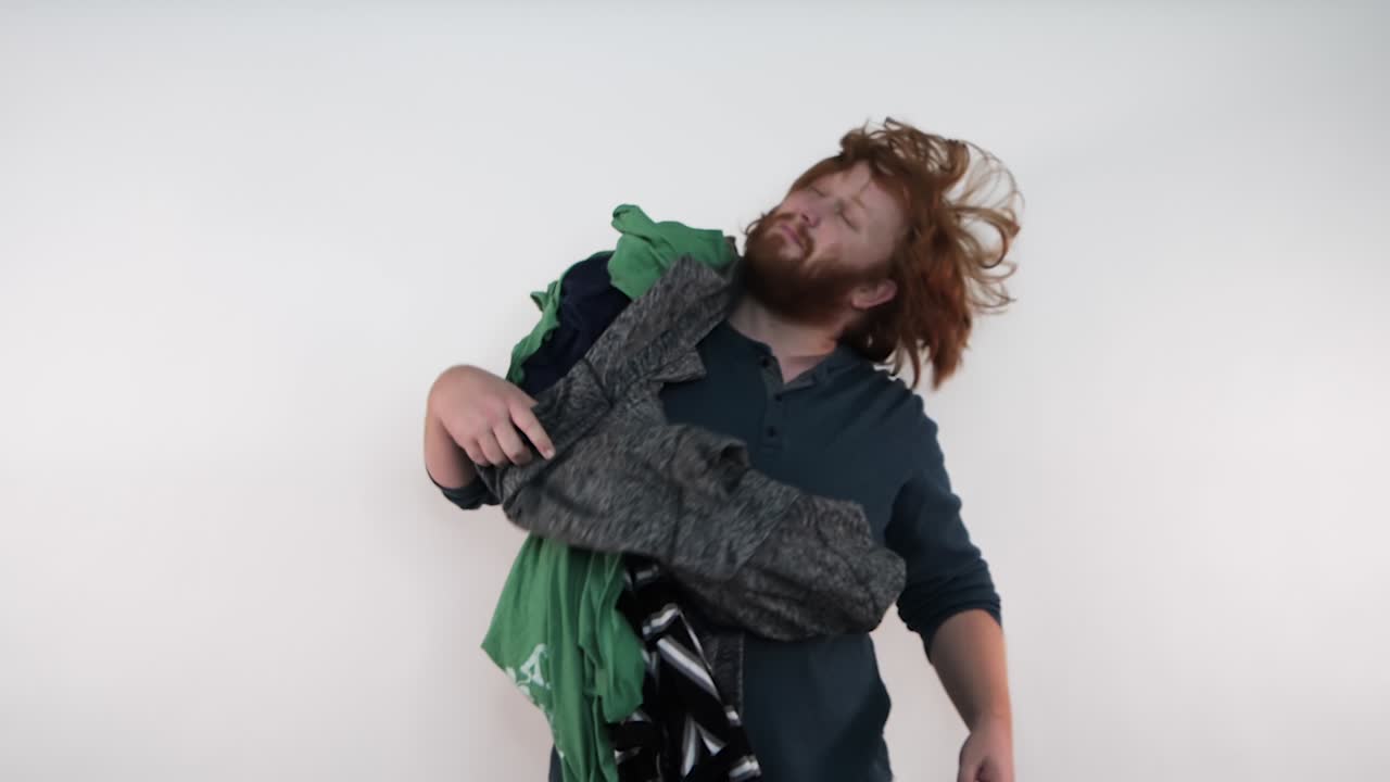 A red-haired man pulling a load of clothes off of his face revealing his smiling face