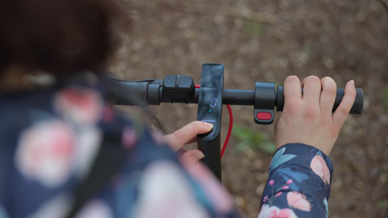 mano femenina presionando el botón de un scooter eléctrico con la otra mano en el manillar