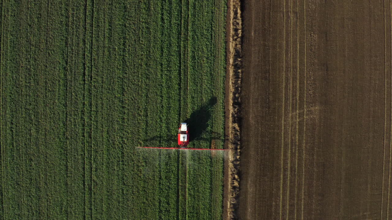 Ripresa aerea dall'alto di un trattore agricolo che irrora un campo con irroratore, erbicidi e pesticidi in una fattoria rurale
