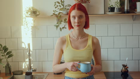 portrait of pretty girl standing in sunlit kitchen, holding coffee mug