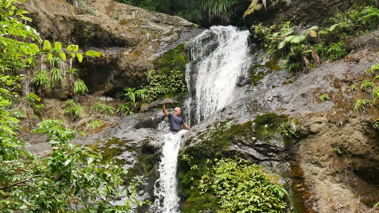 hiker takes selfie video while entering pool at middle of jungle waterfall