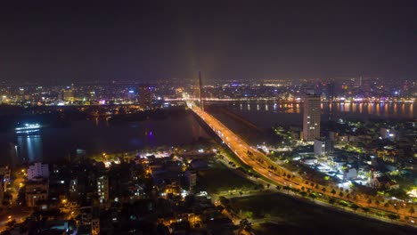 Impresionante-Y-Colorido-Lapso-Nocturno-Aéreo-Del-Icónico-Puente-Tran-Thi-Ly,-El-Tráfico-Y-El-Horizonte-De-La-Ciudad-Cambian-De-Color-En-Danang,-Vietnam