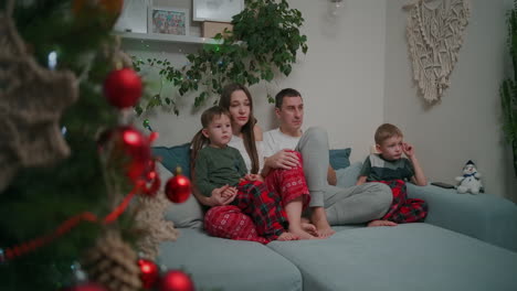 Kaukasische-Familie-Sitzt-Während-Der-Weihnachtsferien-Zusammen-Auf-Einem-Sofa-Und-Schaut-Zu-Hause-Fern-Und-Dekoriert-Die-Wohnungseinrichtung.-Hochwertiges-4K-Filmmaterial