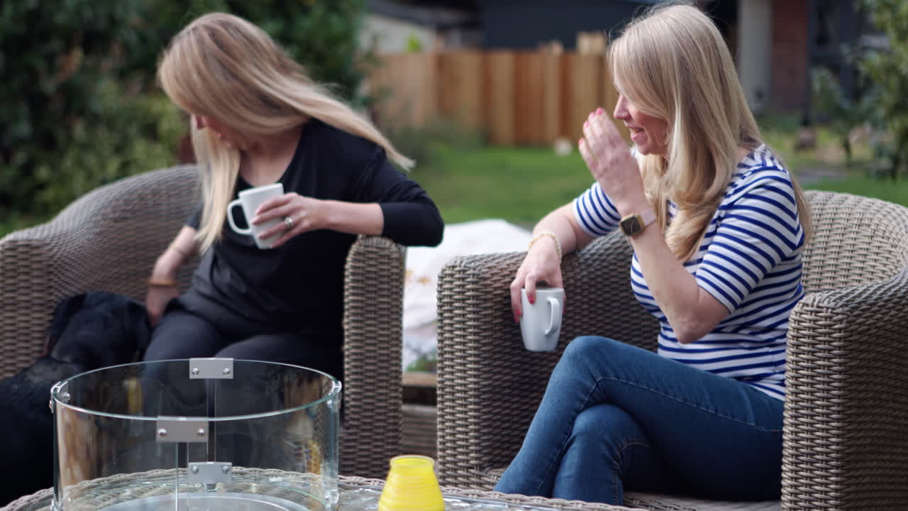 Two women enjoying coffee in a garden with a dog