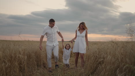 Familia-Feliz-Y-Sonriente-Cogidos-De-La-Mano-Caminando-Por-El-Campo-Dorado-Al-Atardecer.-Familia-Feliz-Caminando-Por-La-Pradera-Y-Jugando.