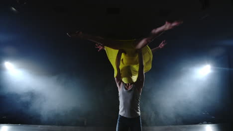 Zoom-camera-two-modern-ballet-dancers-are-dancing-on-stage-in-smoke-a-man-raises-his-partner-in-his-arms-and-rotates-in-the-air.-The-musical-uses-circus-acrobats-dancers.