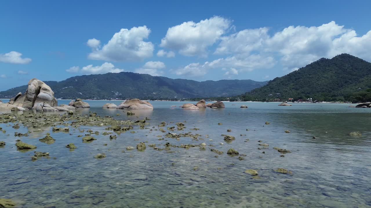 Aerial drone footage of Lamai Beach, Koh Samui, Thailand, showcasing rocky coastline, turquoise ocean water, lush green mountains, and scenic tropical island horizon under a clear sky