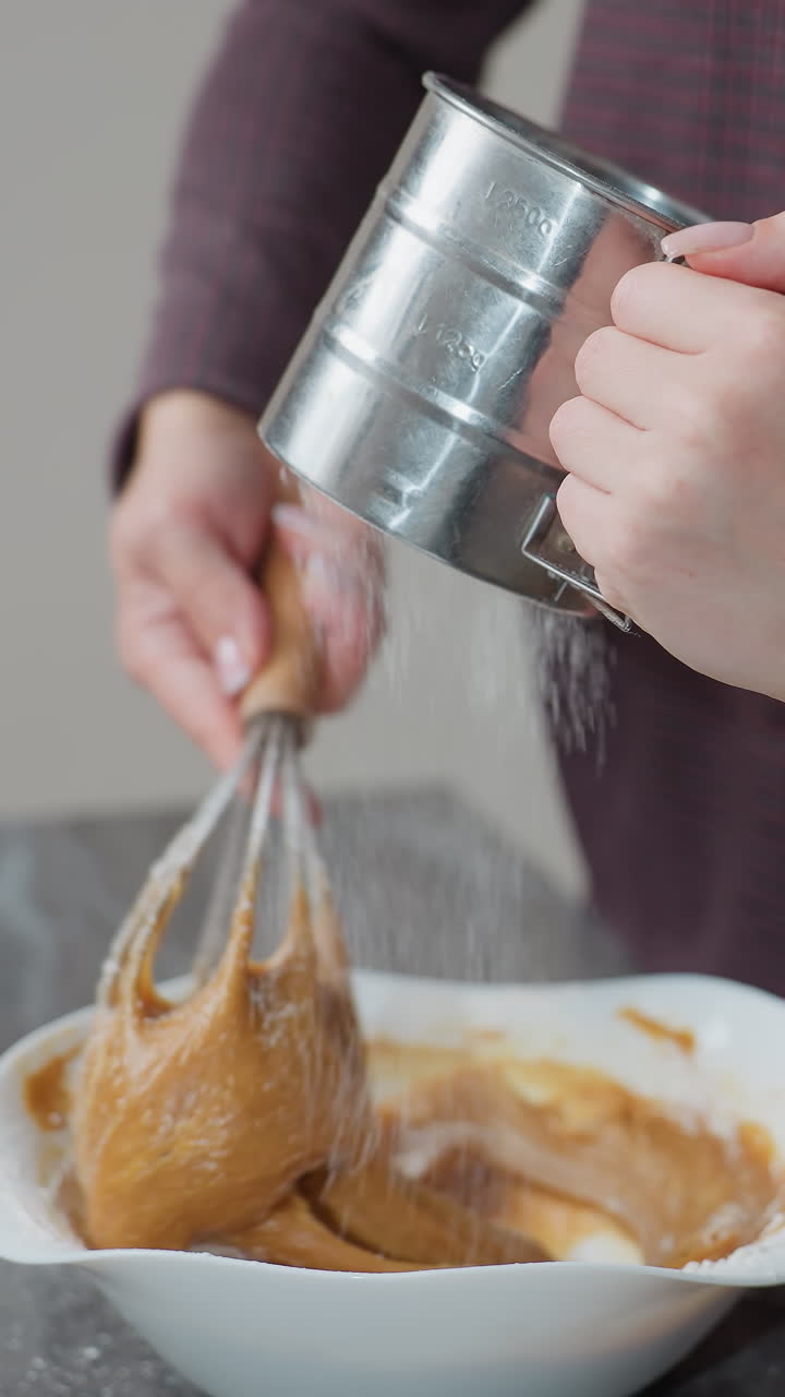 vista parcial de la niña ayudando a su tía en la cocina, sosteniendo un tamiz de metal mientras la tía agita la masa en el arco, trabajan juntos en una cocina brillante y moderna