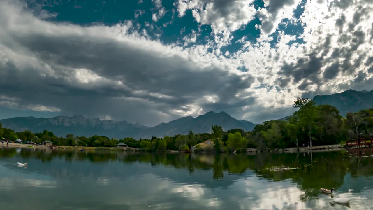 cloudscape reflejándose en el agua en un estanque con montañas rocosas en el fondo - zoom en lapso de tiempo